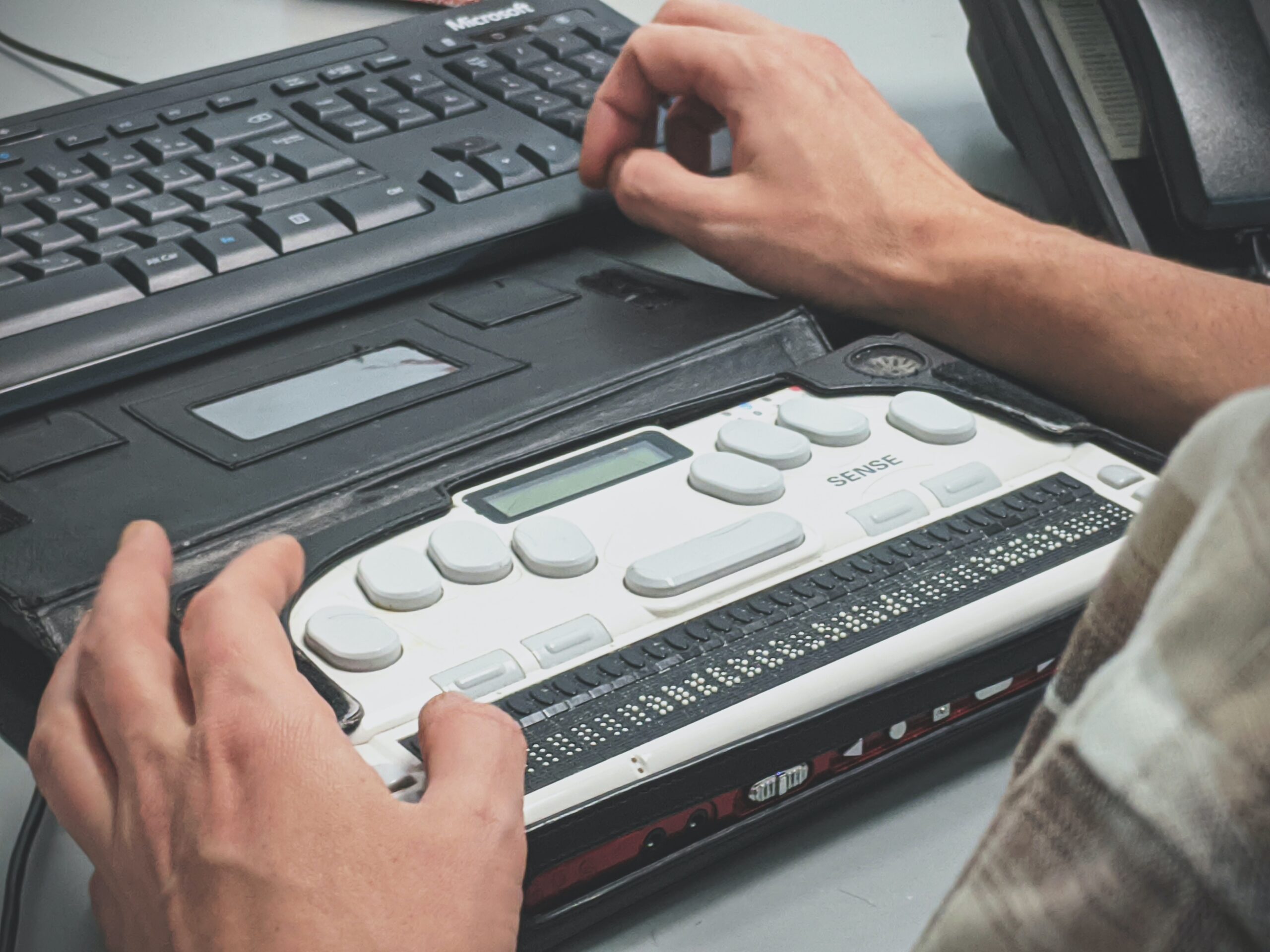 A person uses a braille screen reader and types on a computer keyboard.